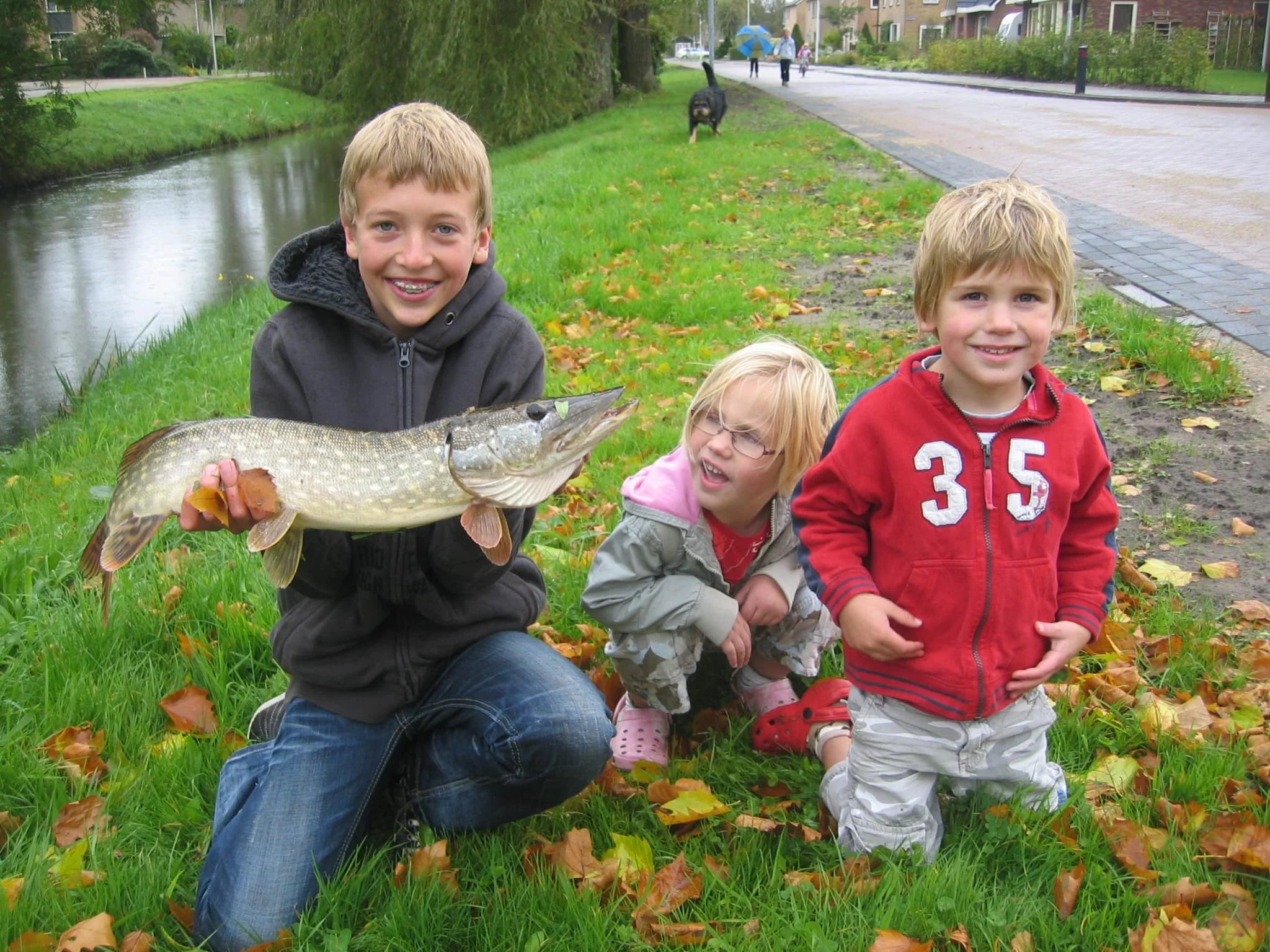 Een jonge Wytse Punter met een vroege snoek, naast zijn jongere broertje en zusje aan een Nederlandse kanaaloever in de herfst