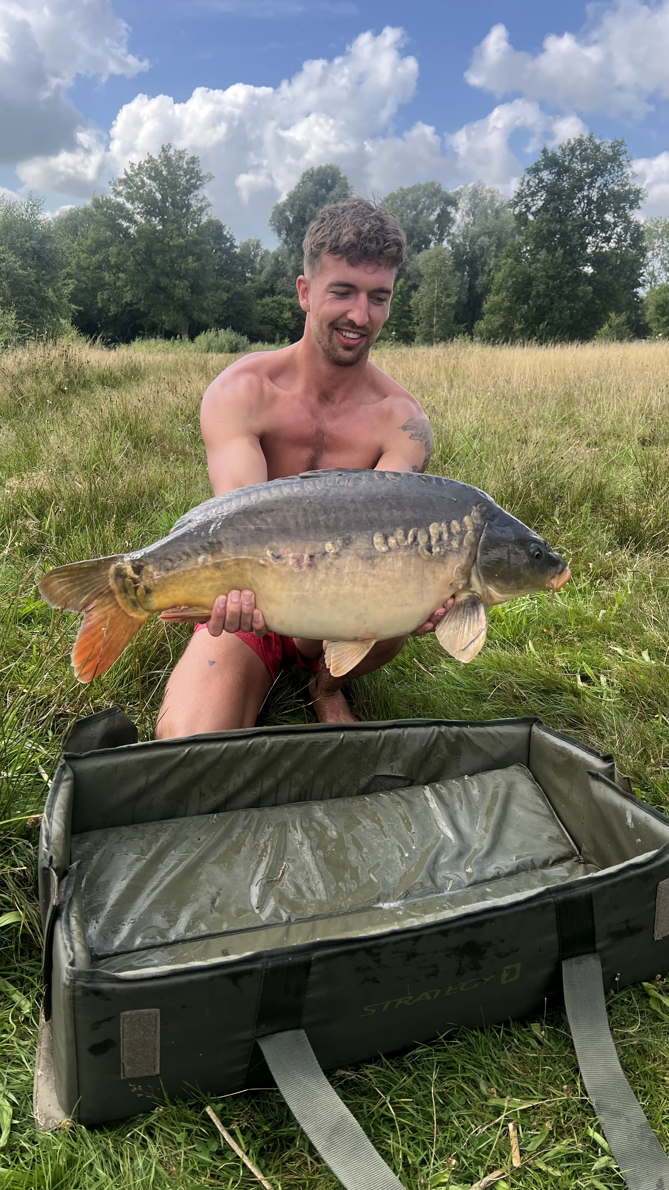 Wytse Punter met een spiegelkarper in een zomerse weide onder een wolkenhemel