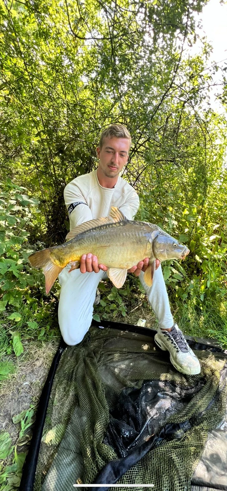 Wytse Punter met een spiegelkarper op de onthaakmat in zomergroen