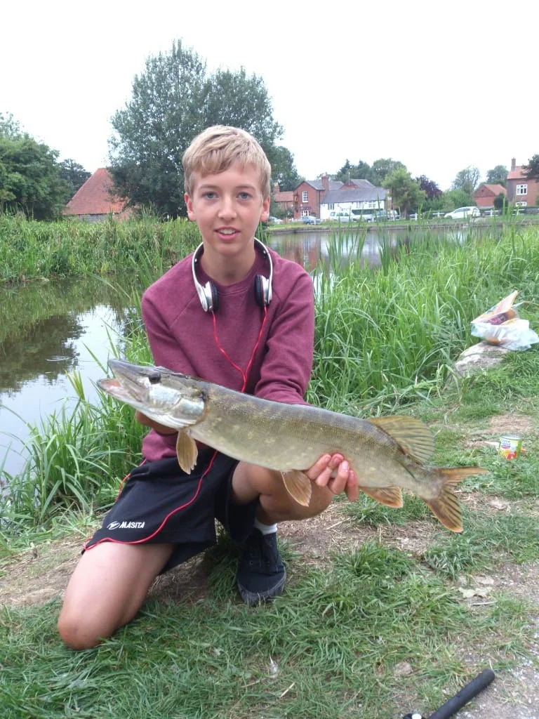 Jonge Wytse Punter met een snoek, met rode koptelefoon op, bij een voorstedelijke vijver